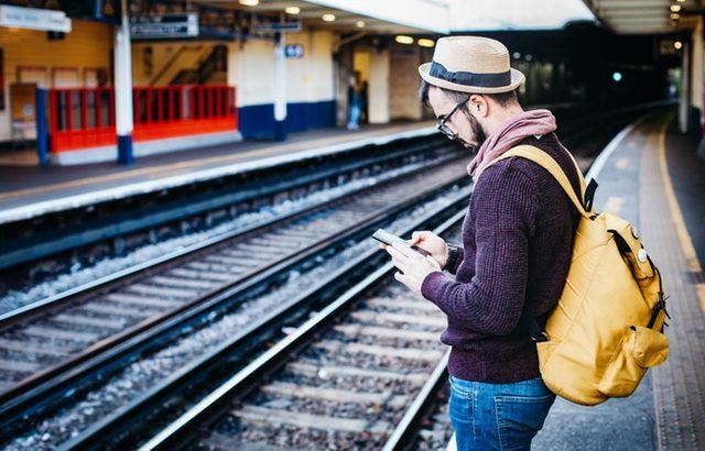 A photograph of a man at the train station looking at his phone | Smarter Travel Limited